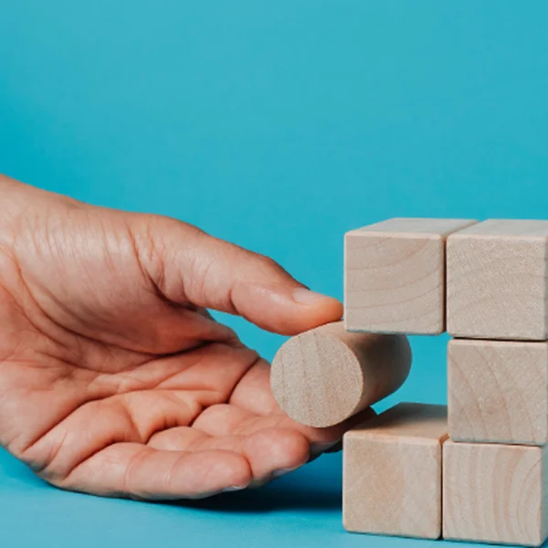 Titel: Strategische Problemlösung in der IT-Beratung

Beschreibung: Eine Hand platziert einen runden Holzblock in einen Würfel aus Holzklötzen, der vor einem hellblauen Hintergrund steht. Dieses Bild symbolisiert innovative Problemlösungen in einer IT-Age