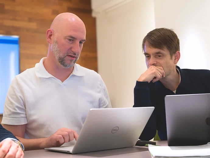 Das Bild zeigt zwei professionelle IT-Berater bei einer Besprechung in einer modernen IT-Agentur. Im Fokus stehen innovative Lösungen und die enge Zusammenarbeit, um maßgeschneiderte IT-Strategien zu entwickeln. Die Verwendung von Laptops deutet auf den E