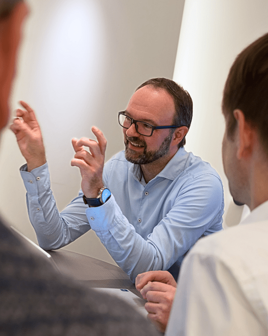 Drei Geschäftspersonen in formeller Kleidung diskutieren angeregt in einem modernen Büro.