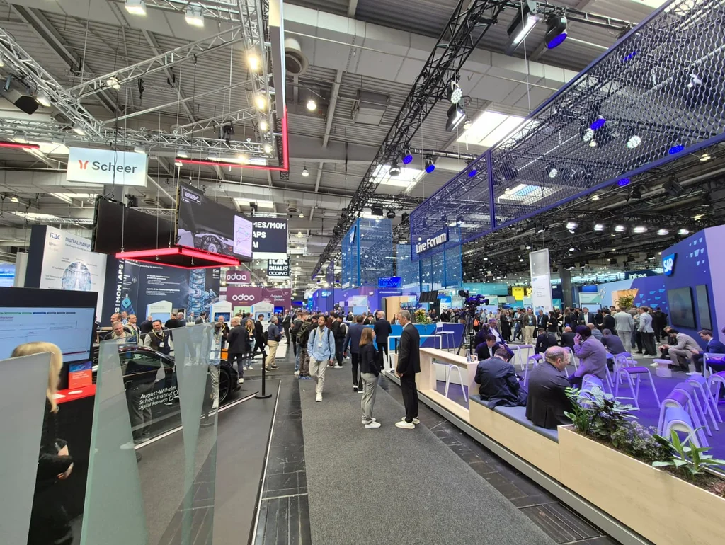 Menschen besuchen eine belebte Messehalle mit verschiedenen Technologie-Ausstellungsständen und digitalen Displays.
