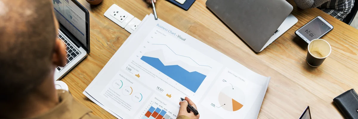 **Bildbeschreibung: Strategiebesprechung in IT-Agentur**

Ein dynamisches Team von Fachleuten in einer IT-Agentur führt eine Strategiebesprechung durch. Auf dem Holztisch sind verschiedene moderne Geräte wie Laptops und Tablets zu sehen, zusammen mit deta