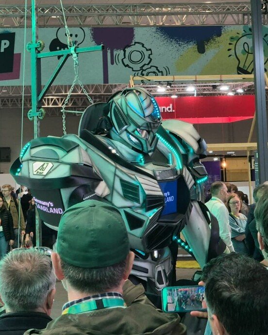 Ein großer humanoider Roboter in einer Messehalle mit "Startup Area" und "Saarland" Schildern, umgeben von Besuchern.
