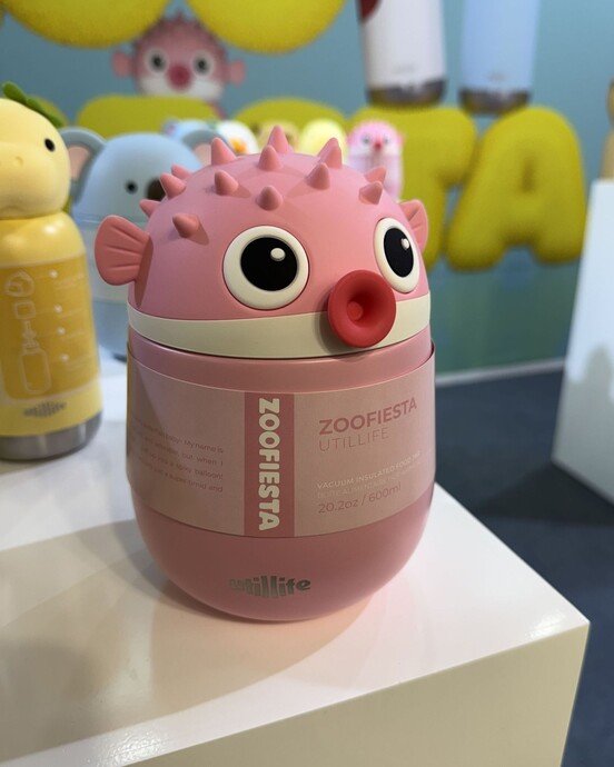 Rosa, kugelförmiger Behälter in Kugelfischform mit großen Augen auf einem weißen Tisch vor unscharfem Hintergrund.