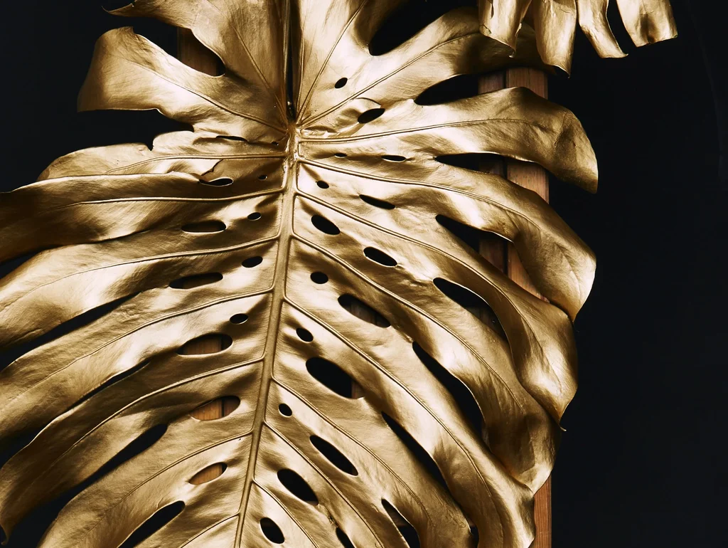 Goldene Monstera-Blätter auf einer Holzleiter vor dunklem Hintergrund.
