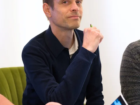 Eine Person sitzt am Tisch und hält einen Stift. Vor ihr liegt ein Tablet.