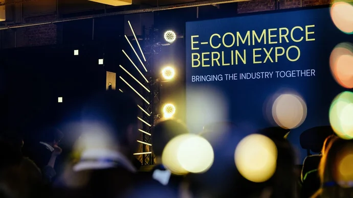 Teilnehmer der E-Commerce Berlin Expo vor einer beleuchteten Bühne mit Slogan "Bringing the Industry Together".