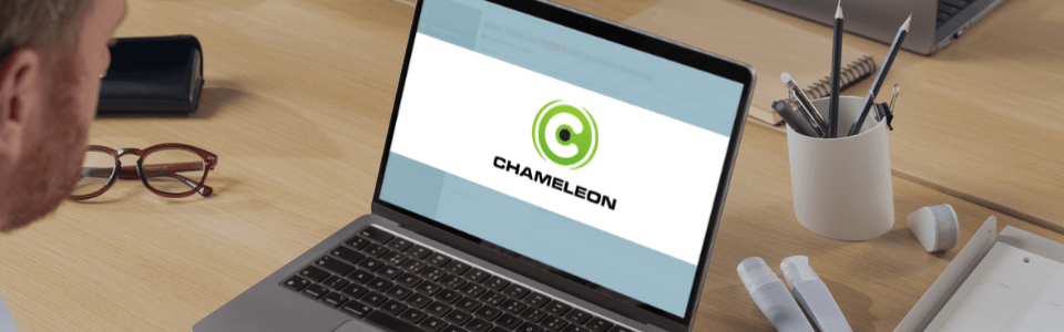 Mann arbeitet an Laptop mit Chameleon-Logo auf dem Bildschirm, im modernen Büroambiente mit Schreibtisch und Pflanzen.