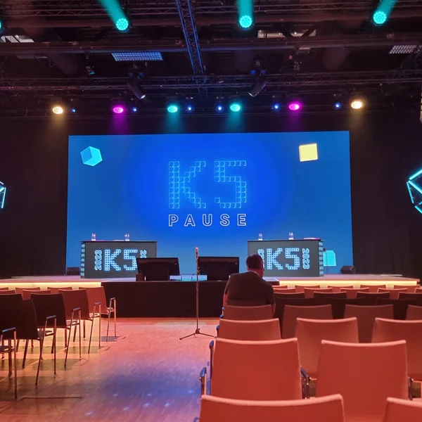 Bühne mit K5-Signage und Sitzreihen; farbige Lichtinstallationen in Würfelform an der Decke.
