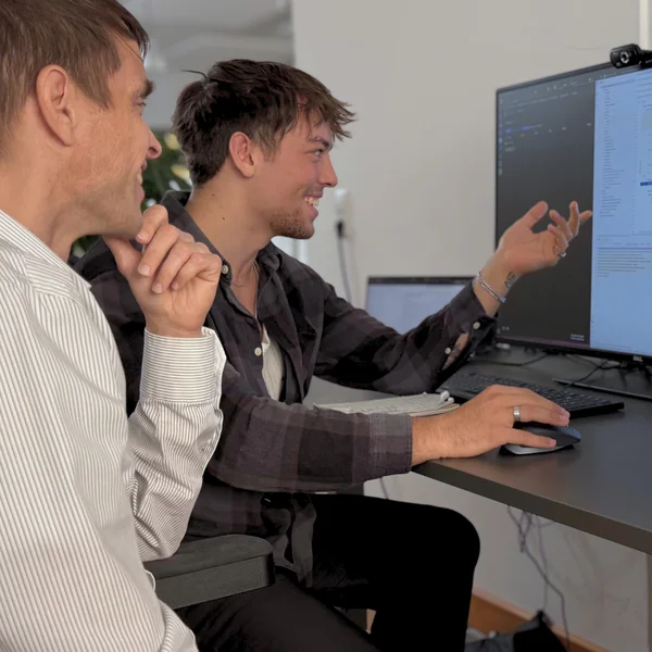 Zwei Männer arbeiten gemeinsam an einem Computerbildschirm in einem Büro und diskutieren vermutlich technische Details.