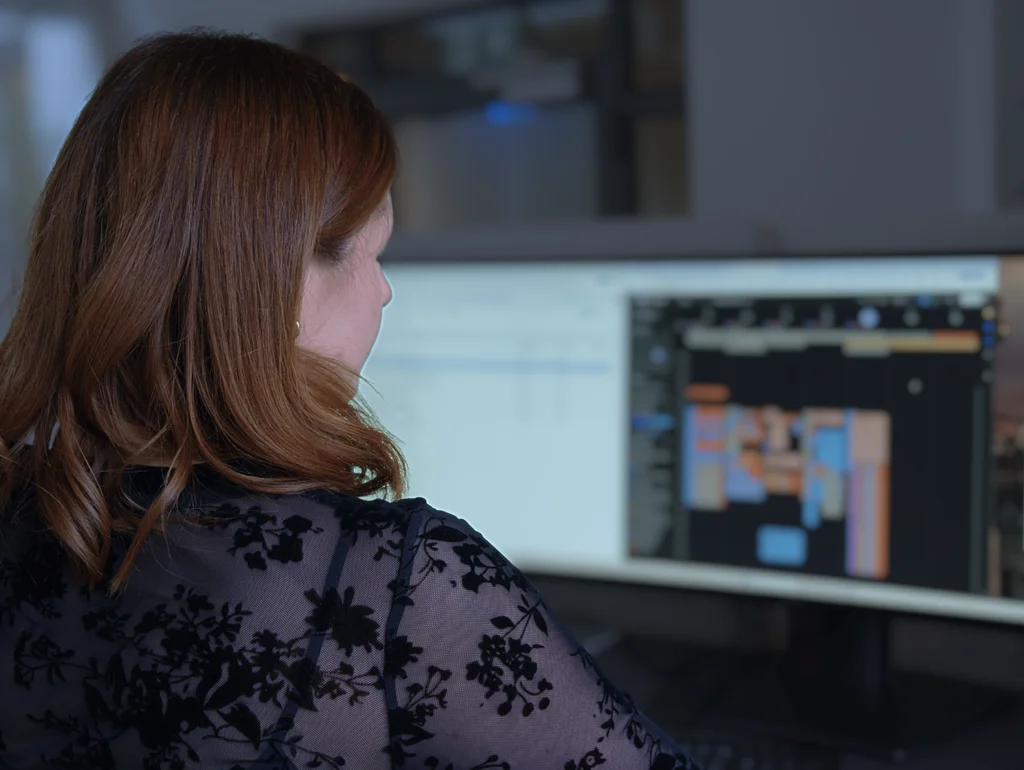 Frau arbeitet an Computerbildschirm mit Diagramm oder Flussdiagramm, trägt schwarze Spitzenbluse.