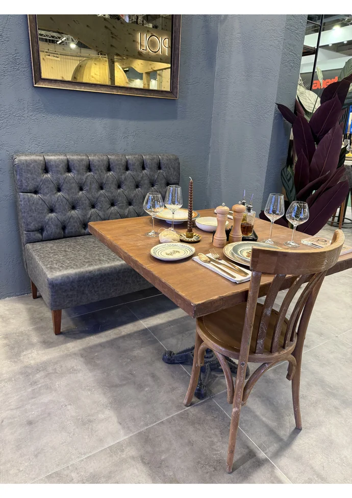 Restauranttisch mit Gedeck: Gläser, Teller, Besteck, Gewürze. Graue Couch, Holzstuhl, moderne Ambiente.