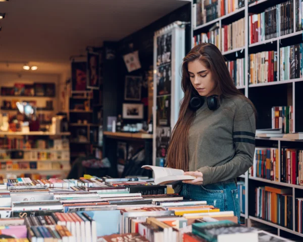Frau liest ein Buch in einer Buchhandlung, umgeben von Bücherregalen und Tischen voller Bücher.