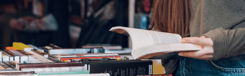 Frau liest ein Buch in einer Buchhandlung, umgeben von Bücherregalen und Tischen voller Bücher.