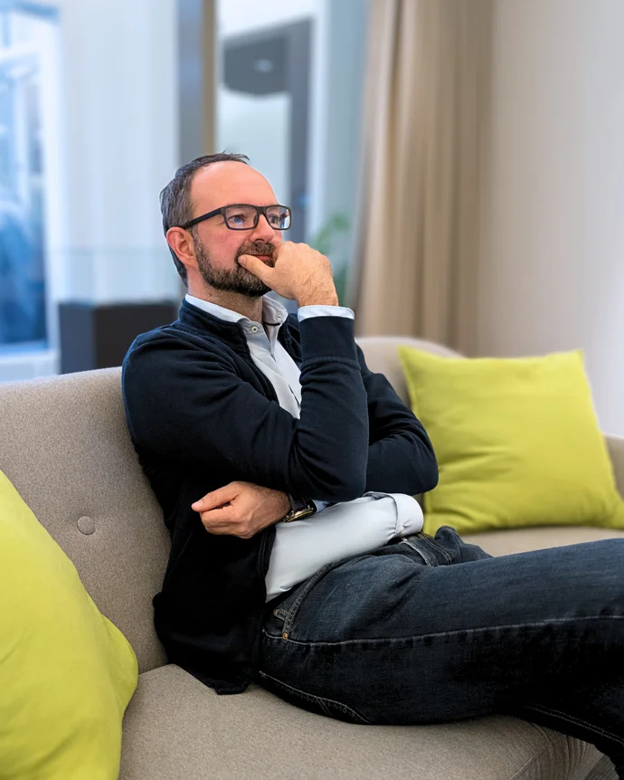 Eine Person sitzt nachdenklich auf einem Sofa mit hellgrünen Kissen im Hintergrund.