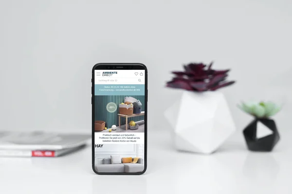 Smartphone vor geometrischen Deko-Objekten, zeigt Website mit Einrichtungsideen. Minimalistisches, modernes Design.
