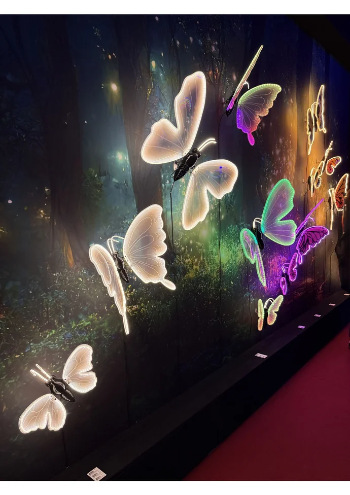 Leuchtende Schmetterlingsinstallationen vor einem mystischen, bewaldeten Hintergrund in verschiedenen Farben.