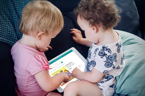 Zwei Kleinkinder interagieren mit einem Tablet auf einem Sofa.