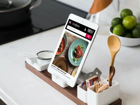 Tablethalter mit Rezeptanzeige, umgeben von Kochutensilien, auf einer Küchenarbeitsfläche.