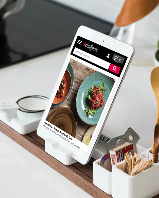 Tablethalter mit Rezeptanzeige, umgeben von Kochutensilien, auf einer Küchenarbeitsfläche.