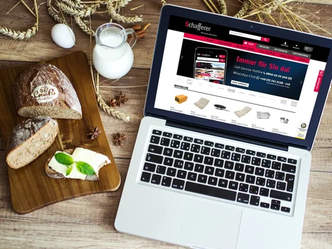 Laptop auf Holztisch mit Brot, Butter und Milch; Website auf dem Bildschirm.