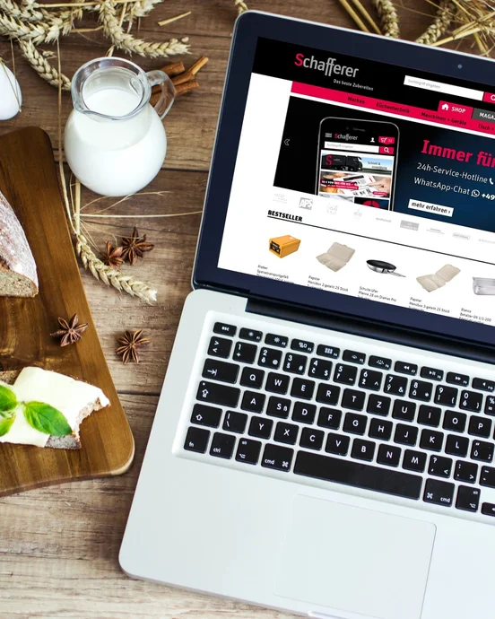 Laptop auf Holztisch mit Brot, Butter und Milch; Website auf dem Bildschirm.