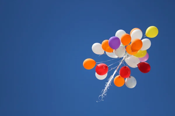 Bunte Luftballons schweben vor wolkenlosem Himmel.