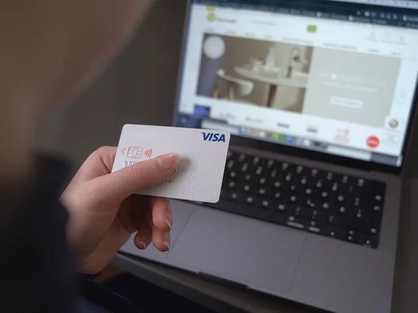 Nahaufnahme einer Person, die online mit einer Kreditkarte auf einem Laptop einkauft. Bildschirm zeigt eine Produktseite.