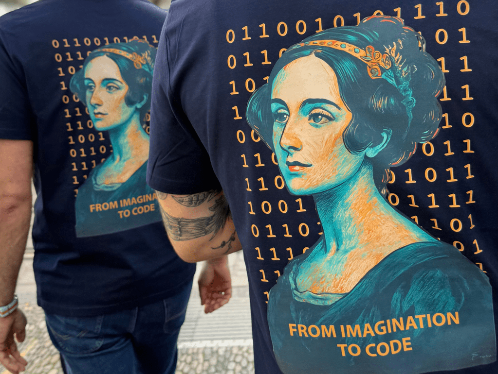 Zwei Personen tragen T-Shirts mit Bild von Ada Lovelace und Binärcode, Aufschrift „From Imagination to Code“.