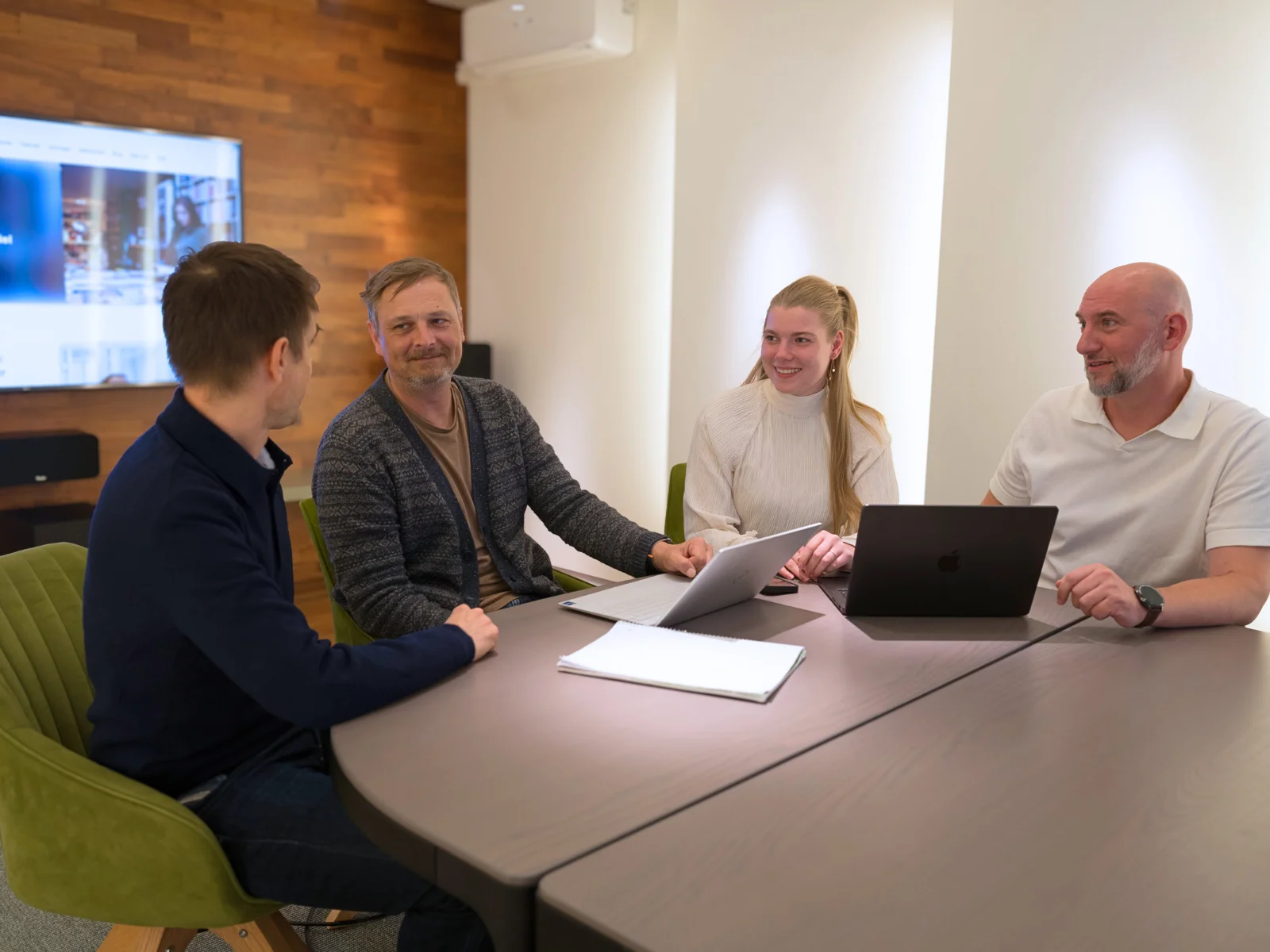 Personengruppe in einem modernen Besprechungsraum mit Laptops und Notizen, engagiert in einer Diskussion.&nbsp;