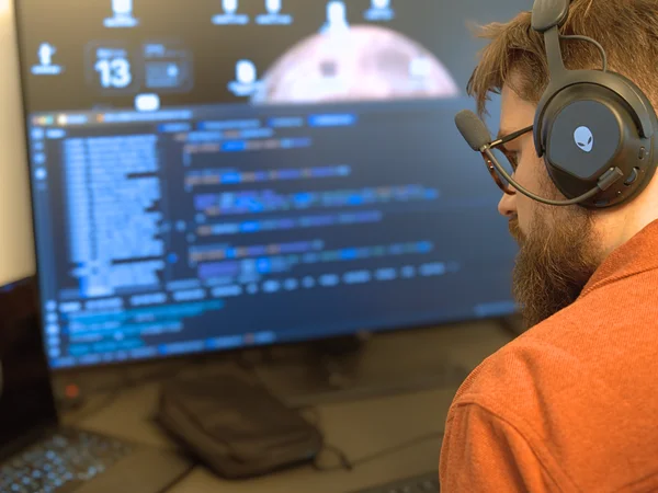 Ein Mann mit Headset arbeitet an einem Computerbildschirm mit komplexem Code.