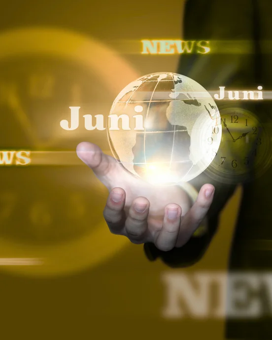 Hand hält leuchtende Weltkugel mit "Juni" und "News" in goldenem Hintergrund. Uhr leicht sichtbar, symbolisiert Aktualität.