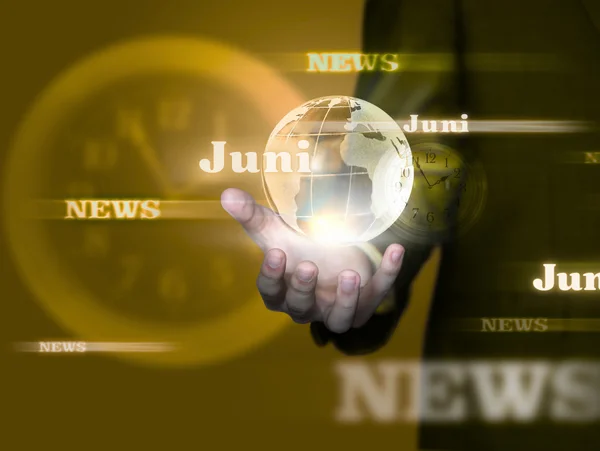 Hand hält leuchtende Weltkugel mit "Juni" und "News" in goldenem Hintergrund. Uhr leicht sichtbar, symbolisiert Aktualität.