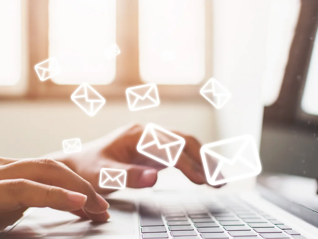 Hände tippen auf Laptop, umgeben von schwebenden E-Mail-Symbolen, die digitale Kommunikation darstellen.