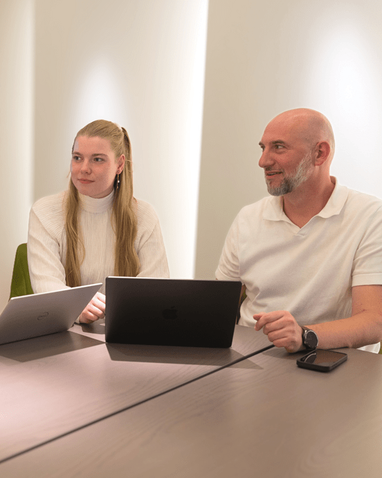 Vier Personen diskutieren an einem ovalen Tisch mit Laptops in einem modern beleuchteten Besprechungsraum.