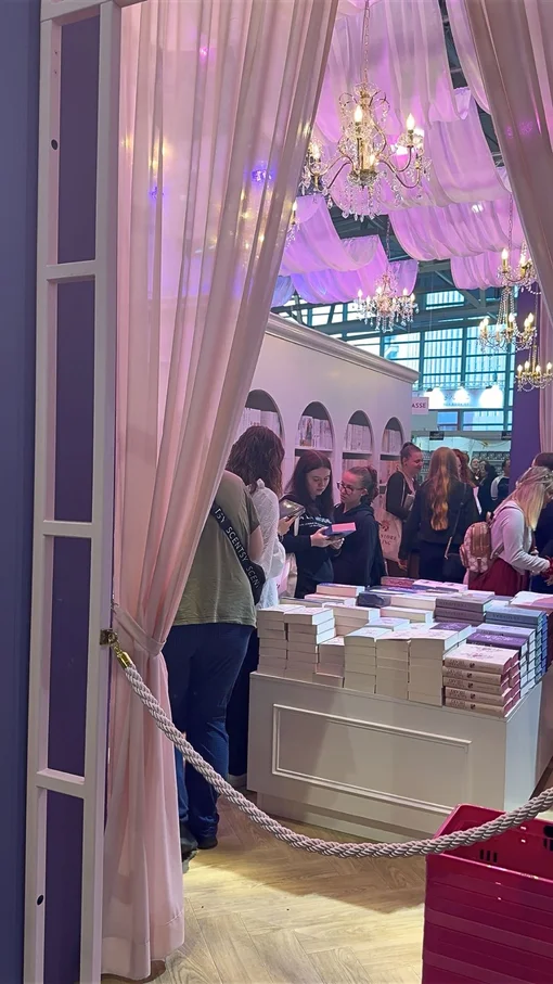 Ein Messe-Stand mit dekorativen Elementen, Büchertisch und mehreren Personen in einer Halle.
