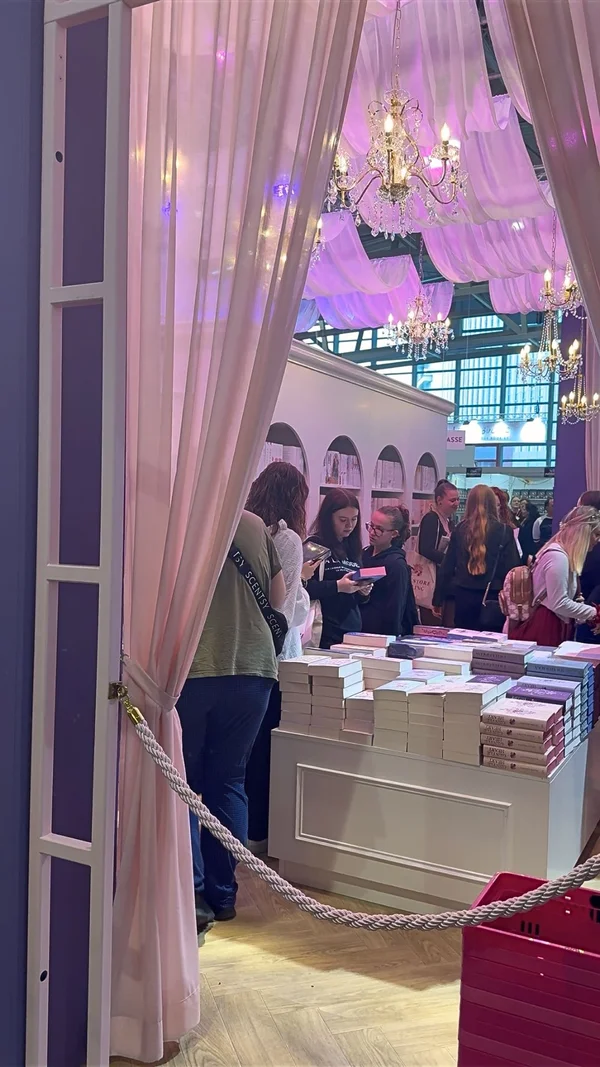 Ein Messe-Stand mit dekorativen Elementen, Büchertisch und mehreren Personen in einer Halle.