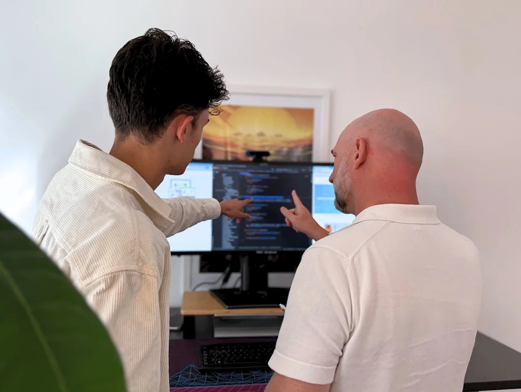Zwei Männer diskutieren und zeigen auf Code auf einem Computerbildschirm in einem Büro.