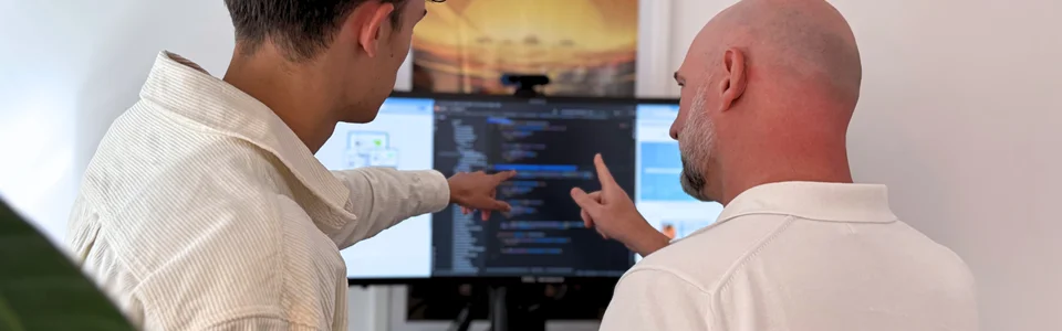 Zwei Männer diskutieren und zeigen auf Code auf einem Computerbildschirm in einem Büro.