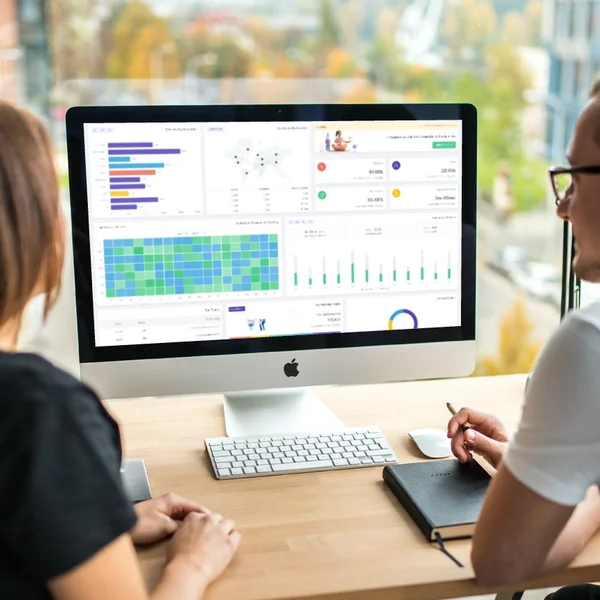 Zwei Personen analysieren Datenvisualisierungen auf einem Computerbildschirm in einem modernen Büro.