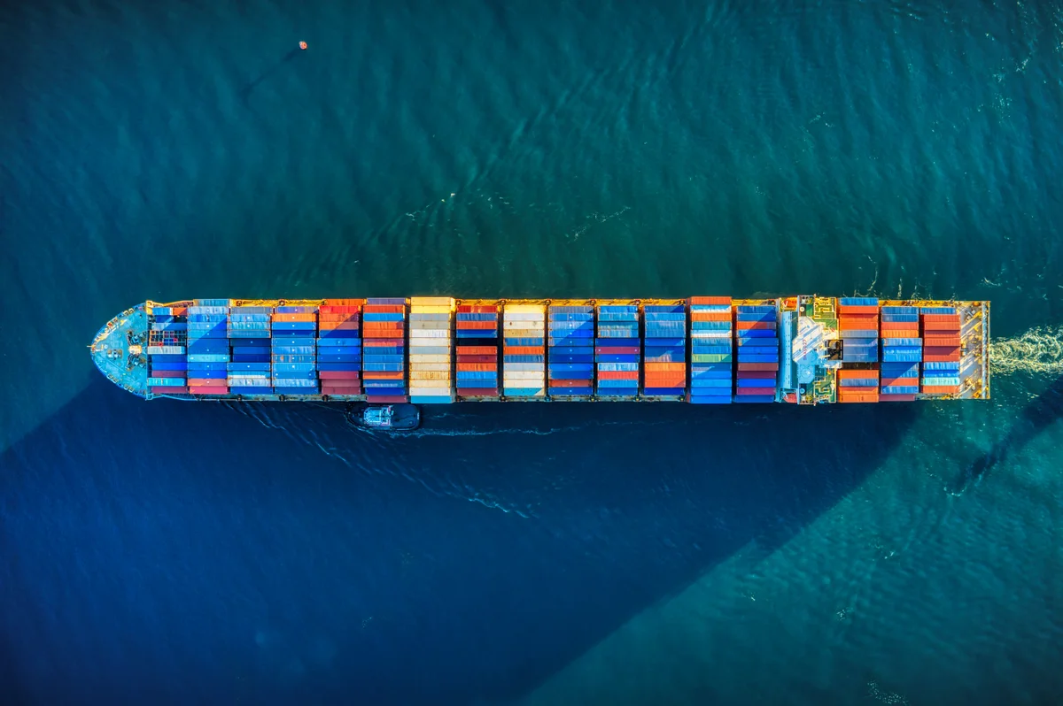 Luftaufnahme eines fahrenden Containerschiffs mit bunten Frachtcontainern im Meer.