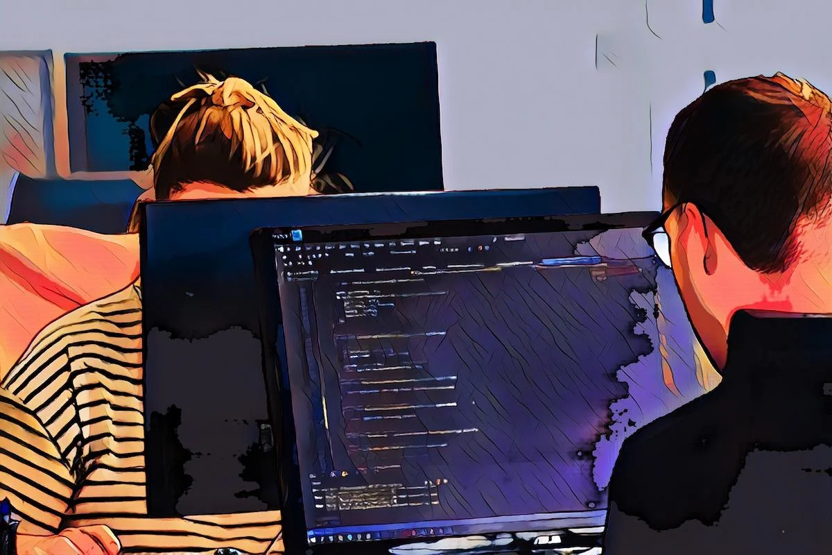 Zwei Personen arbeiten an Computern, einer zeigt Code auf dem Bildschirm.