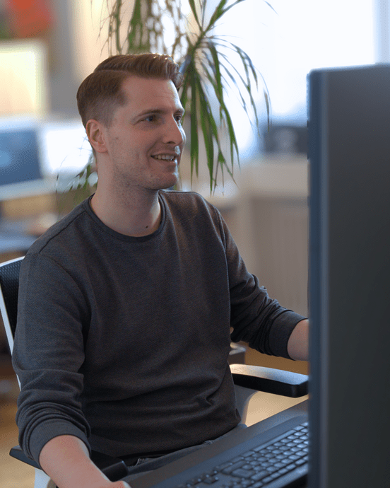 Person am Schreibtisch arbeitet konzentriert an einem Computerbildschirm in einem Büro.