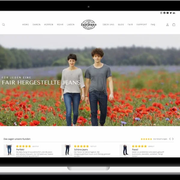 Laptop mit geöffneter Webseite, auf der zwei Personen durch ein Mohnfeld spazieren. Text "Fair hergestellte Jeans".