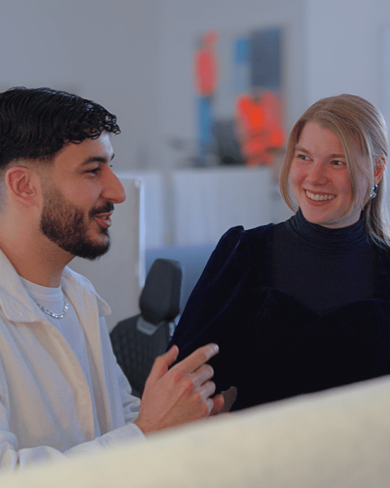 Zwei Personen unterhalten sich in einem Büro, umgeben von modernen Arbeitsplätzen und technischer Ausstattung.