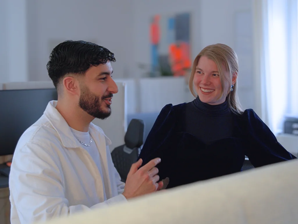 Zwei Personen unterhalten sich in einem Büro, umgeben von modernen Arbeitsplätzen und technischer Ausstattung.