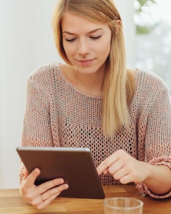 Junge Frau nutzt ein Tablet in einem modernen Wohnraum, mit Fokus auf Interaktion und Technologie.