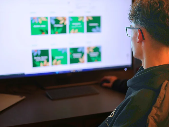 Person am Computer betrachtet bunte Bilder auf einem großen Monitor bei geringer Beleuchtung.
