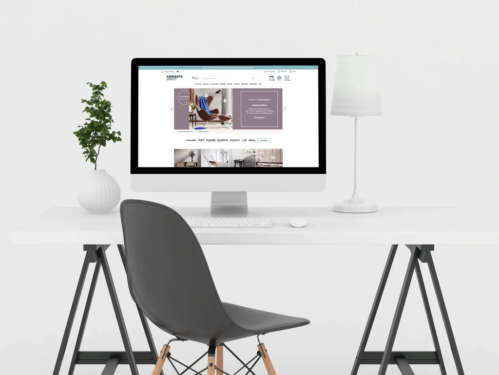 Moderner Schreibtisch mit Computer, schwarzem Stuhl, weißer Lampe und Pflanze vor weißem Hintergrund.