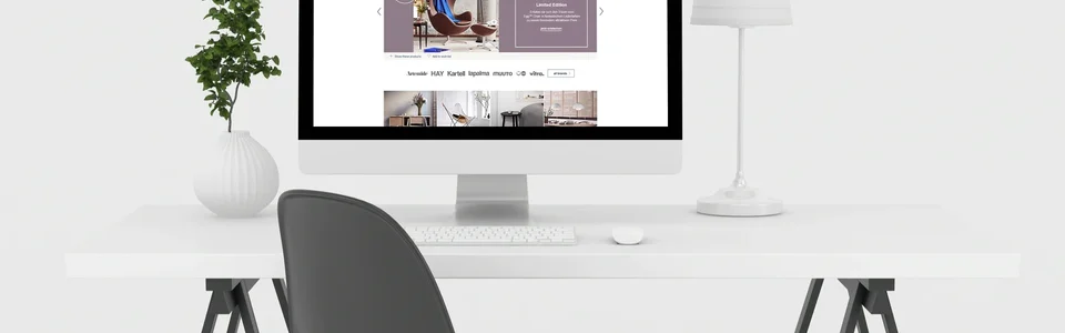 Moderner Schreibtisch mit Computer, schwarzem Stuhl, weißer Lampe und Pflanze vor weißem Hintergrund.