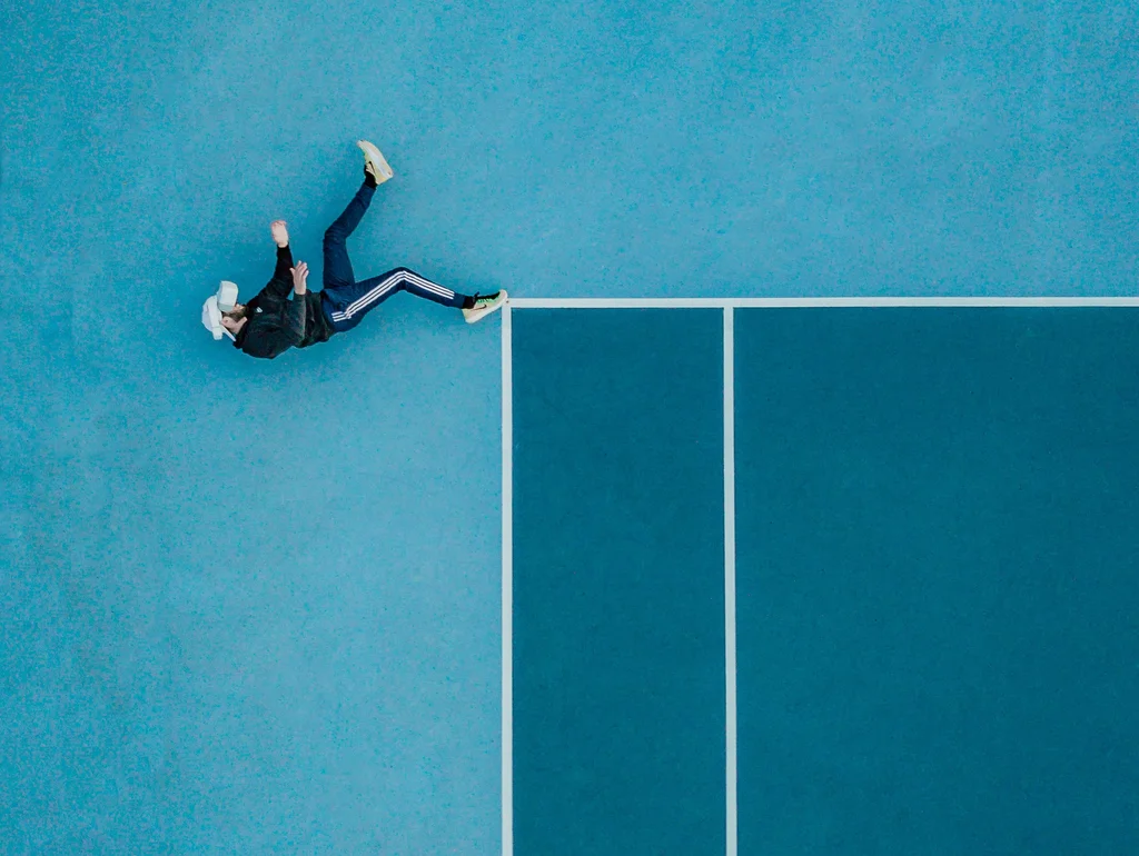 Person auf blauer Tennisplatzfläche liegend, aus Vogelperspektive.